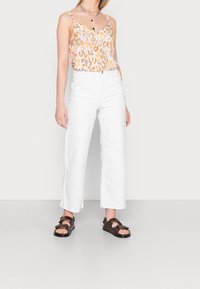 Top recortado de estampado de leopardo en naranja y beige, combinado con vaqueros de pierna ancha blancos de cintura alta. Sandalias marrones con tiras texturizadas.