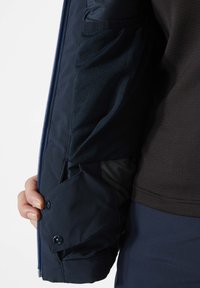 Navy-Jacke mit Reißverschluss und Knopfverschluss, ausgestattet mit Netzstecktaschen und glattem Stoff, der komplizierte Nähte und ein mehrlagiges Design zeigt.