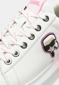 Λευκό αθλητικό παπούτσι με λείο δερμάτινο επάνω μέρος, ροζ λεπτομέρειες, στρογγυλή μύτη και μαύρα κορδόνια. Διαθέτει λογότυπο καρτούν στο πλάι.