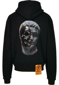 Svart hettegenser med et grafisk design av et delt ansikt, som kombinerer en marmor skulptur og et svart kranium, med et merket oransje merke.