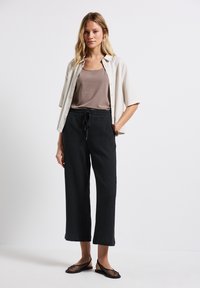 Svarta texturerade vida byxor med elastisk midja, tillsammans med en ljus beige kortärmad skjorta över en brun tank top, och svarta mesh-skor.