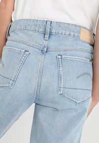 Ljusblå denimjeans med hög midja, som har två bakfickor och en brun läderlogotyp på baksidan till höger.