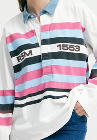 Herrenhemd mit Kragen und langen Ärmeln in Weiß mit pinken, blauen und schwarzen Streifen; mit "RSM 1553" auf der Vorderseite bedruckt, aus Baumwollmaterial.