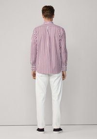 Herrenhemd mit rot-weißem Streifenmuster, aus Baumwollstoff, mit Button-Down-Kragen, langen Ärmeln, kombiniert mit weißen Hosen und marineblauen Schuhen.
