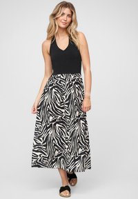 Robe maxi avec un haut sans manches noir et une jupe fluide présentant un motif zèbre blanc et noir. Des sandales plates noires complètent le look.