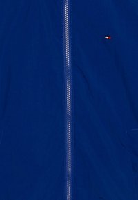 Giacca a vento blu con chiusura full zip, tessuto strutturato e un piccolo logo ricamato sul lato superiore sinistro.