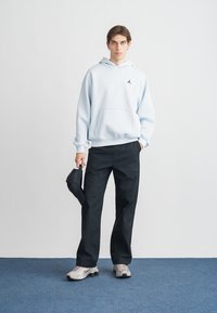 Sweat à capuche bleu clair avec poche kangourou et logo noir, associé à un pantalon noir et des baskets grises. Accessoire incluant une casquette noire.
