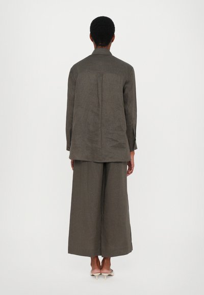 Σκούρο πράσινο κοστούμι δύο τμημάτων που περιλαμβάνει ένα φαρδύ, μακρυμάνικο τοπ και παντελόνι με φαρδιά πόδια, φτιαγμένα από υφασμάτινη υφή.