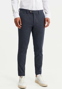 Kalhoty tmavě modré texturované látky se slim fit, se zapínáním na knoflík a poutky na opasek, doplněné bílými teniskami.