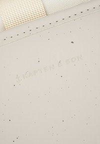 Světle béžová taška s hladkým texturovaným povrchem, která má jemný vzor teček. Název značky "KAPTEN & SON" je vyražen.