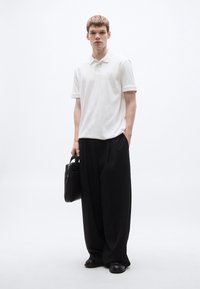 Fehér rövid ujjú pólóing, laza fekete nadrág és fekete bőr táska. Simább textúrák, minimalista design és semleges színek dominálnak.