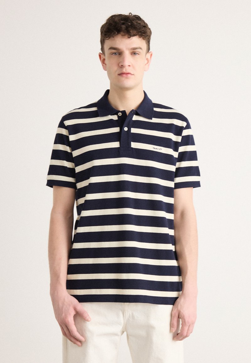 Navy og kremstripete polo skjorte med krage og korte ermer. Har en liten brodert logo på venstre side. Myk stofftekstur.