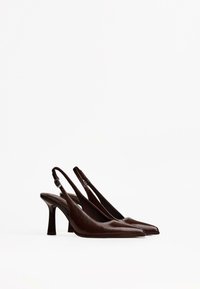 Brown leather slingback heels with pointed toes and a tapered heel. Features a smooth texture and adjustable ankle strap for fit.