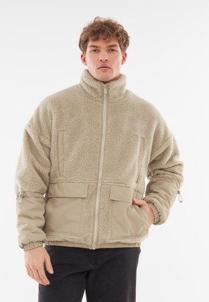 Tanjacket van fleece met een hoge kraag, rits aan de voorkant en twee borstzakken. Elastische mouwen en een trekkoord aan de onderkant. Zacht, gestructureerd materiaal.
