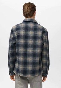Károvaná bunda v námorníckej modrej a béžovej farbe, vyrobená z texturovanej tkaniny, s golierom a zapínaním na gombíky na rukávoch. Zadný pohľad zobrazuje štvorcový vzor a rovný lem.