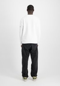 Felpa bianca con polsini e orlo a costine, dotata di etichetta nella parte posteriore del collo e tasca laterale. Abbinata a jeans grigi scuri dal taglio morbido e sneakers.