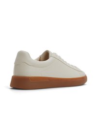 Zapatilla de cuero blanca con perfil bajo, puntera redondeada, suela de goma marrón y acentos texturizados en el talón y los lados. Diseño con cordones.