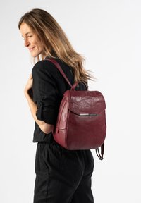 Bordeauxfarbener Leder-Rucksack mit runder Form, Klappenverschluss und silbernen Hardware-Akzenten. Verfügt über verstellbare Schulterriemen.