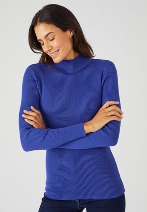 Maglione lungo a maniche lunghe a coste blu con un collo alto, design aderente e texture morbida. Braccia incrociate in vita, con una vestibilità slim.