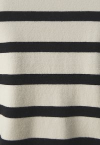 Gestreifter Pullover in Creme und Schwarz; verfügt über horizontale Streifen in unterschiedlichen Breiten. Die Textur wirkt weich und leicht flauschig.