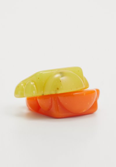 Puscaidīgas krāsas, sakrautas ziepes dzeltenā un oranžā krāsā. Dzeltenā ziede ir gluda ar redzamām pūkām; oranžā ir izliekta ar noapaļotiem akcentiem.