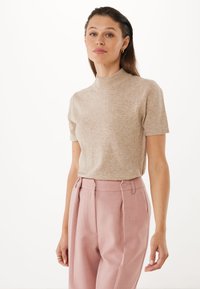 Beige pletený top s krátkým rukávem a vysokým výstřihem, kombinovaný s přizpůsobenými světle růžovými kalhotami s předními plizé a knoflíkovými detaily.