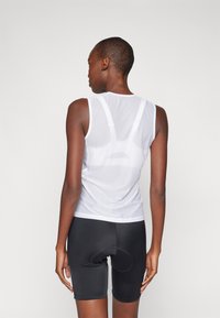 Hvit nettingtank topp med racerback-design, kombinert med svarte tettsittende shorts med polstret sete. Glatt tekstur og atletisk passform.
