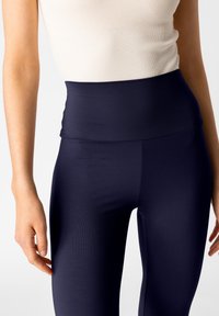 Leggings a vita alta di colore navy realizzati in materiale elasticizzato, con una texture liscia e un design aderente, ideali per comfort e libertà di movimento.