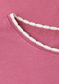 Encolure ronde d'un vêtement en maille rose avec bordure blanche festonnée le long du bord, montrant une texture côtelée fine et des détails de couture.