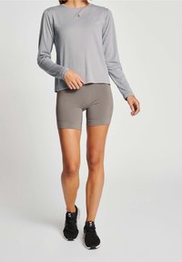 Langärmliges graues Sportoberteil, kombiniert mit grauen Shorts, mit Rundhalsausschnitt und tailliertem Schnitt, getragen mit schwarzen Sport Schuhen.