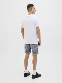 Hvid bomulds t-shirt, grå denim shorts, rullede ærmer, sorte sko, hvide sokker, set fra ryggen mod en neutral baggrund.