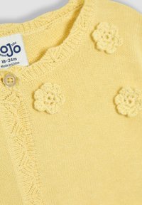 Žltý pletený cardigan so zaobleným výstrihom, vyšitými akcentmi v tvare kvetu a zapínaním na gombík. Na etikete je uvedená veľkosť 18-24 mesiacov.