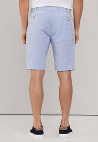 Shorts rayés bleu et blanc avec une taille élastique et deux poches arrière ornées de boutons dorés, portés avec des chaussures noires à enfiler.