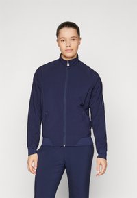 Navy bomber jacket with a high collar, full zip, side pockets, and textured sleeves. Lightweight material, streamlined design, athletic fit.