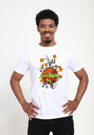 Smilende mand iført en hvid t-shirt med Bugs Bunny, Daffy Duck og andre Looney Tunes-figurer med basketballer og teksten "Space Jam".
