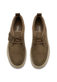 Scarpe in suede marrone con punta arrotondata, design con lacci e linguetta superiore. Suola in gomma testurizzata di colore beige chiaro in contrasto.