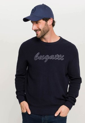Mørkeblå striktrøje med "bugatti" broderet i lysegrå. Sammen med en matchende mørkeblå kasket med et logo.