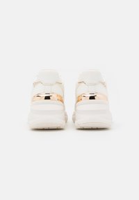 Paire de baskets à plateforme blanches avec des accents en or rose brillant au niveau du talon, vues de dos sur un fond blanc uni.