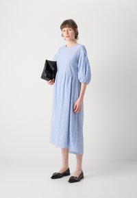 Stripet blå og hvit midi-kjole med pufferm, rund hals og samlet midje. Kombinert med en svart clutch og svarte leppestift.