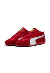 Rote Wildleder- und Stoff-Sneaker mit weißem Seitenstreifen, schwarzem Rand und gelbem Logopatch auf den Zungen, im Dreiviertelansicht dargestellt.