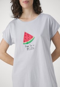 Camiseta cinza-claro de mangas curtas com um gráfico de uma fatia de melancia com sementes pretas e casca verde, texto embaixo: "Um em Mil."