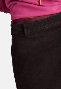 Černé kordové kalhoty se žebrovanou texturou a vínovým pasem, na kterém se opakuje nápis "UNITED COLORS OF BENETTON".