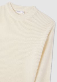 Kremowy sweter dziewiarski o prążkowanej fakturze i okrągłym dekolcie. Materiał wydaje się miękki i lekko gruby.