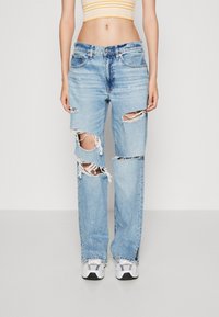 Jeans de color azul claro con desgastes y bordes deshilachados, de corte holgado y con múltiples cortes en las rodillas. Combinados con zapatillas deportivas blancas y negras.