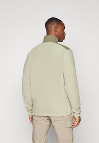 Chaqueta de forro polar en verde claro con cuello alto, que presenta mangas largas y un corte holgado. Textura suave y diseño minimalista.