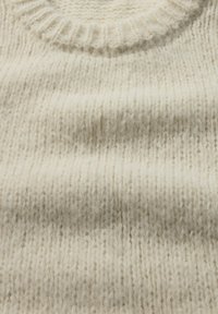 Crèmekleurige gebreide trui met een ribbelrand en een zachte, gestructureerde stof met zichtbare stikpatronen.