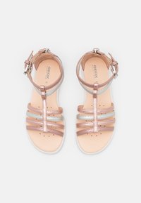 Sandalias de tiras en oro rosa metálico y plateado con cierre de hebilla, puntera abierta y plantilla perforada transpirable. Diseño de suela plana.