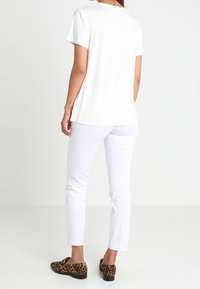 Hvid kortærmet t-shirt med en afslappet pasform, parret med hvide tapered bukser og brune leopardmønstret slip-ons.