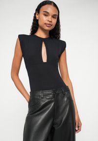 Bodysuit preto com mangas curtas e recorte em forma de chave no centro, combinado com calças de couro pretas de cintura alta com bolsos frontais.