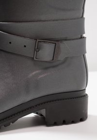 Grijze leren laars met een gladde textuur, voorzien van een brede riem en een rechthoekige gespsluiting, dikke zool met grip.